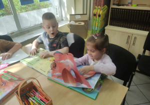 Zdjęcie przedstawia dwoje dzieci przeglądających książki. Jedno z nich patrzy z zachwytem na zawartość książki.