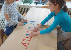 Na zdjęciu widać dziewczynki, które tworzą napis autyzm