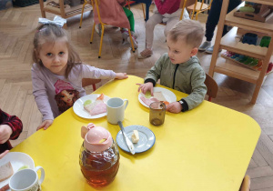 Zdjęcie przedstawia dzieci siedzące przy stoliku. Dzieci przygotowują sobie śniadanie.