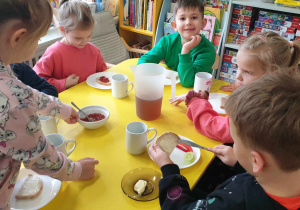 Zdjęcie przedstawia dzieci siedzą przy stoliku. Dzieci przygotowują sobie samodzielnie śniadanie.