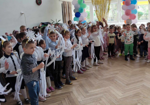 Zdjęcie przedstawia dzieci stojące w półkole, które śpiewają piosenkę.