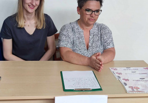 Zdjęcie przedstawia dwie kobiety siedzące za biurkiem z napisem jury.