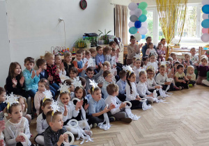 Zdjęcie przedstawia dzieci siedzące w pólkole, dzieci klaszczą w dłonie.