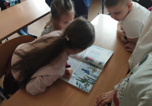 Na zdjęciu widzimy dwie dziewczynki z grupy I i chłopca z klasy I, który pokazuje im książke i wspólnie próbują przeczytać wyrazy.