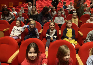 Zdjęcie przedstawia dzieci siedzące w fotelach na sali teatralnej.
