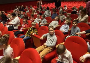 Zdjęcie przedstawia dzieci siedzące w fotelach na sali teatralnej.