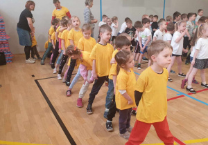 Zdjęcie przedstawia dzieci ubrane w żółte podkoszulki. Dzieci czekają na rozpoczęcie zabaw sportowych.
