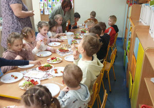 Zdjęcie przedstawia dzieci siedzące przy stole. Dzieci jedzą koreczki.