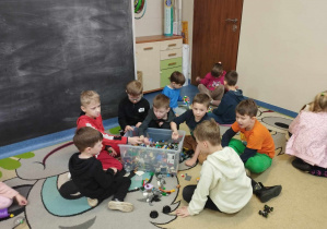 Zdjęcie przedstawia kilku chłopców siedzących na dywanie. Chłopcy układają klocki lego.