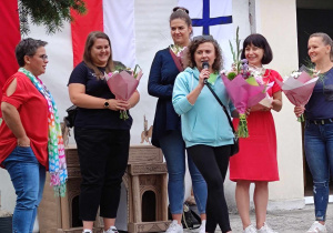 Zdjęcie przedstawia panią dyrektor oraz rodziców z kwiatami. Jedna z kobiet przemawia przez mikrofon.