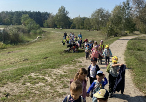 Zdjęcie przedstawia dzieci idące w parach przez polanę.