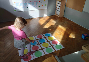 Na zdjęciu widzimy dziewczynkę, która pokonuje drogę skacząc po odpowiednich kolorach kropek wylosowanych na kostce.