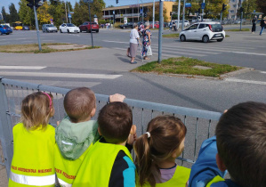 Na zdjęciu widzimy grupkę dzieci, które patrzą i obserwują co dzieje się na skrzyżowaniu.