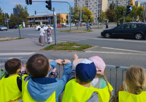 Na zdjęciu widzimy grupkę dzieci, które patrzą i obserwują co dzieje się na skrzyżowaniu.