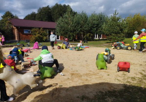 Na zdjęciu widzimy grupkę dzieci, które bawią się w dużej piaskownicy.