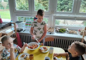 Na zdjęciu widzimy grupkę dzieci, które jedzą sałatkę owocową.