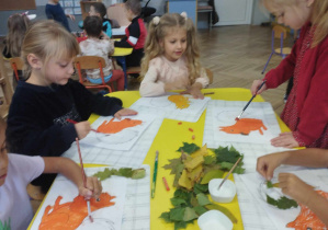 Na zdjęciu widzimy grupkę dzieci, które wykonują pracę plastyczną.