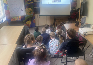 Zdjęcie przedstawia dzieci oglądające film edukacyjny na rzutniku.