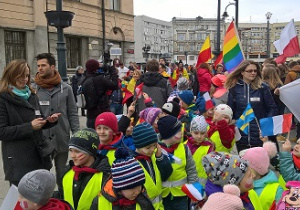 Na zdjęciu widać wolontariusza i grupę przedszkolaków z flagami różnych narodowości podczas marszu