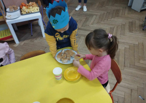 Na zdjęciu widzimy dziewczynkę, która czestuje się ciastem.