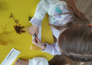 Na zdjęciu widzimy dziewczynkę, która z naturalnego materiału tworzy zakładkę.