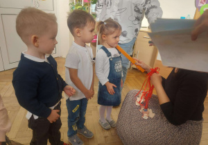 Zdjęcie przedstawia kobietę, która kładzie kredkę na ramieniu dziewczynki- pasuje ją na przedszkolaka.