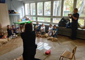 Na zdjęciu widzimy grupkę dzieci, które ćwiczą składanie rąk przygotowując się do uciskania klatki piersiowej poszkodowanego misia.