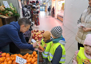 Zdjęcie przedstawia jak dzieci kupują owoce i warzywa w warzywniaku