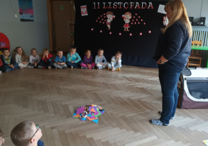 Pani instruktor stoi na środku sali, a dzieci siedzą w kole.