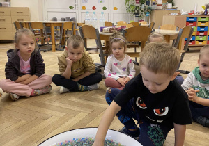 Zdjęcie przedstawia chłopca wkładającego rękę do miski z kulkami.