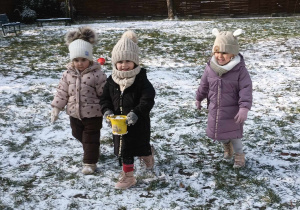 trzy dziwczynki jedna z nich trzyma wiaderko ze śniegiem