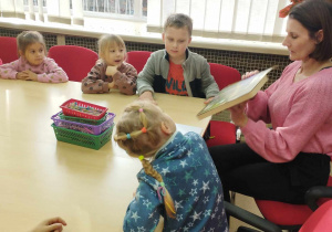 Na zdjęciu widzimy grupkę dzieci i Panią bibliotekarkę, która czyta im bajkę o jeżyku.