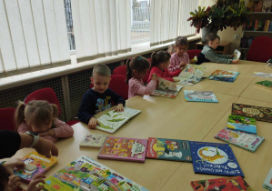 Na zdjęciu widzimy grupkę dzieci, które oglądają książki z biblioteki.