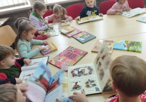 Na zdjęciu widzimy grupkę dzieci, które oglądają książki z biblioteki.