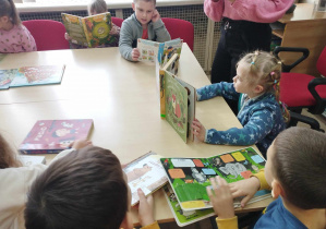 Na zdjęciu widzimy grupkę dzieci, które oglądają książki z biblioteki.