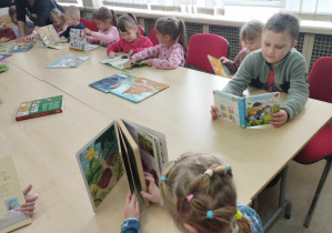 Na zdjęciu widzimy grupkę dzieci, które oglądają książki z biblioteki.