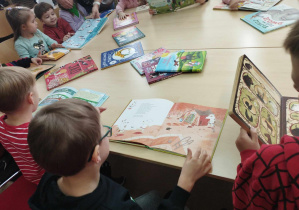 Na zdjęciu widzimy grupkę dzieci, które oglądają książki z biblioteki.