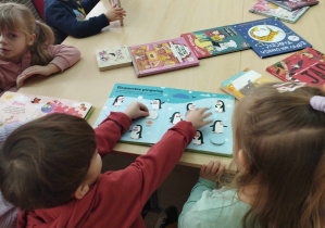 Na zdjęciu widzimy grupkę dzieci, które oglądają książki z biblioteki.