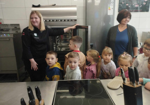 Na zdjęciu widzimy panią nauczycielkę ze Szkoły, która pokazuje dzieciom piec i inne kuchenne przedmioty.