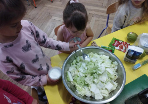 Na zdjęciu widzimy dziewczynkę, która soli kapustę znajdującą się w misce.