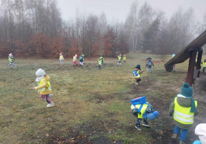 Zdjęcie przedstawia dzieci biegające po polanie.