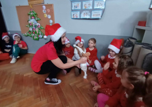 Zdjęcie przedstawia dzieci siedzące w kole oraz panią dyrektor trzymającą w ręku maskotkę renifera, witającego się z dziećmi.