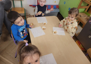 Zdjęcie przedstawia dzieci siedzące przy stoliku i jedzą babeczki.