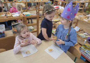 Zdjęcie przedstawia tzry dziewczynki siedzące przy stoliku. Dzieci jedzą babeczki.