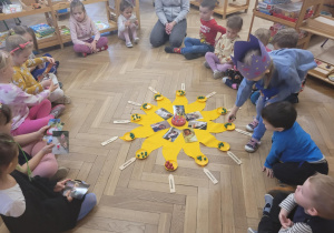 Zdjęcie przedstawia słońce montesoriańskie i dzieci siedzące w kole, oglądajace zdjęcia.