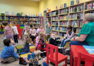 Zdjęcie przedstawia dzieci na zajęciach w bibliotece. Dzieci słuchają o zasadach korzystania z biblioteki.