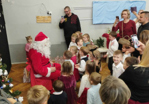 Na zdjęciu widzimy grupkę dzieci, które stoją koło Mikołaja.