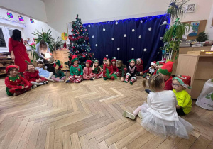 Zdjęcie przedstawia dzieci siedzące w półkolu, w strojach z przedstawienia/