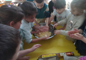 Na zdjęciu widzimy grupkę dzieci, które tworzą małe kuleczki.