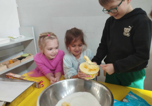 Na zdjęciu widzimy chłopca, który wkłada do miski margarynę. Dziewczynka siedząca koło chłopca pomaga mu, trzymając opakowanie.